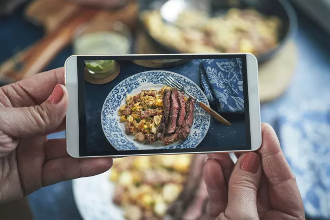 A student takes a picture of a plate of food with their cell phone for Online Culinary Arts Operations