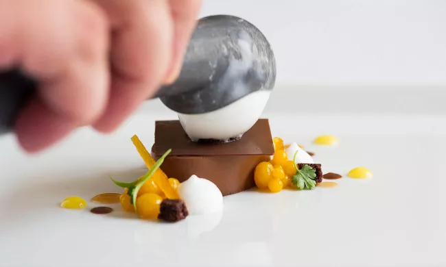 An ICE pastry arts student plates a chocolate dessert with sorbet