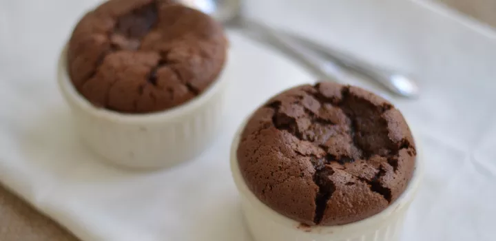 Two chocolate souffles in white ramekins sit on a white plate
