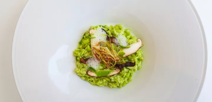 Green edamame risotto topped with mushrooms and fried leeks sits in a white plate