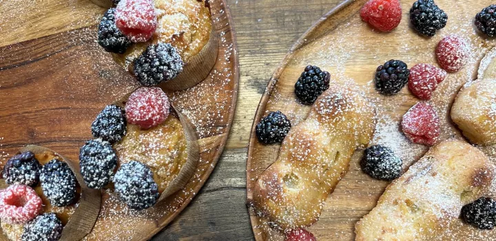 Muffins and mini cakes dusted with powdered sugar and garnished with berries sit on wooden plates