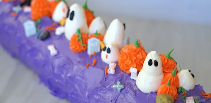 Pumpkin and ghost buttercream decorations on top of a purple cake