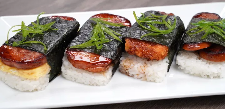 Four pieces of musubi sit on a white plate