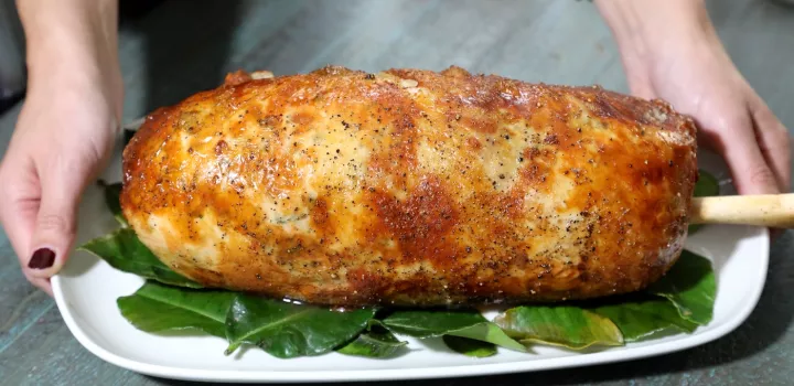 A large turkey roulade roast with a bone sticking out of the end sits on a white plate