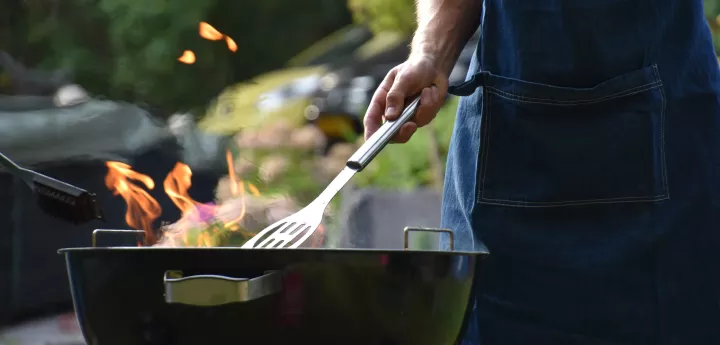 A person uses a spatula to cook outside on a fiery grill
