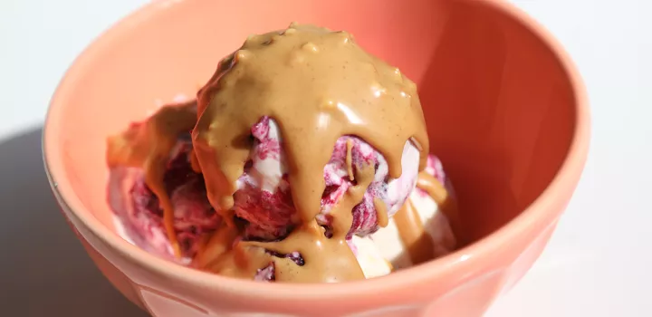 Concord grape ice cream topped with peanut butter sauce in a pink bowl