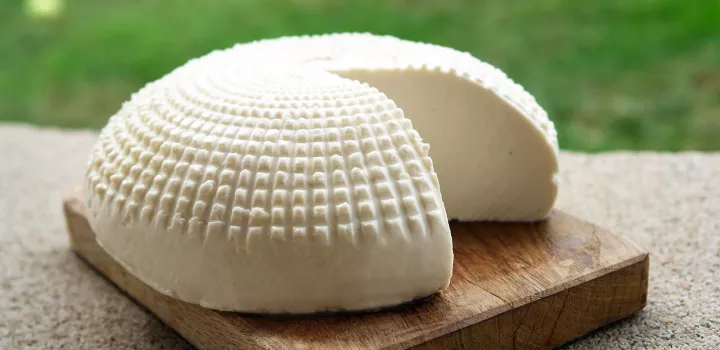 A wheel of goat cheese with a piece cut out sits on a wooden board
