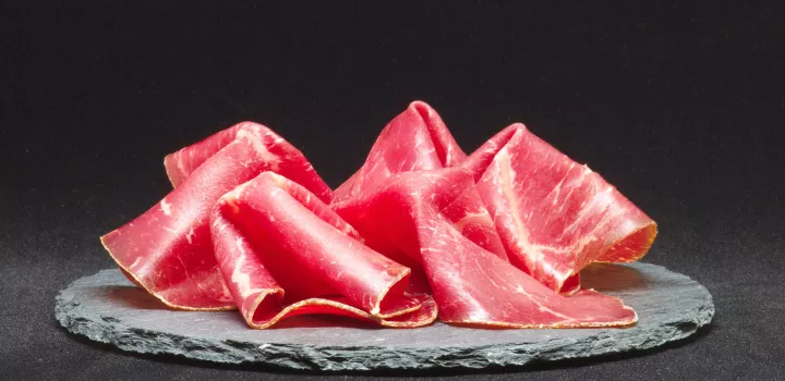 Slices of ham sit on a black plate in front of a black background