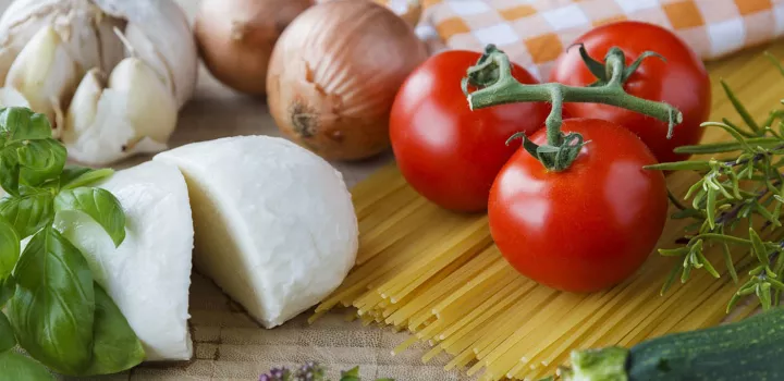 Fresh mozzarella, tomatoes, onions, pasta and garlic sit on a wooden surface