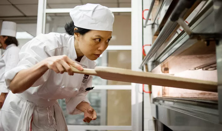 A culinary instructor removes bread from an oven.