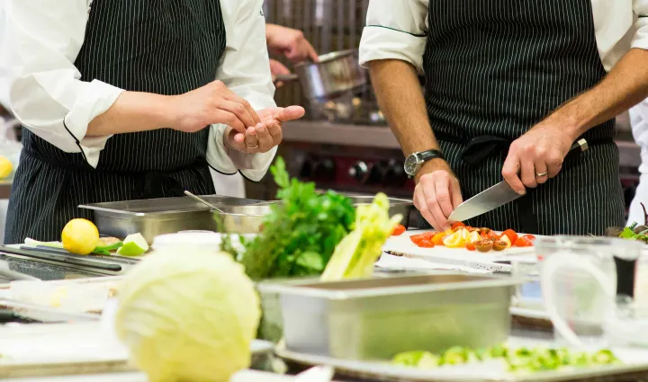 Two chefs work in a kitchen with black striped aprons
