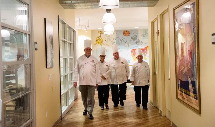ICE instructors walk down a culinary school lobby decorated with framed ICE awards