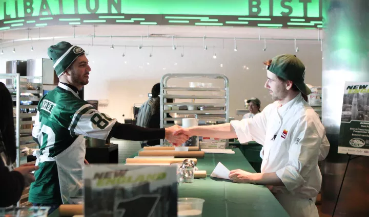 An ICE chef and a New York Jets fan shake hands at MetLife Stadium before an Official Jets Cooking School class