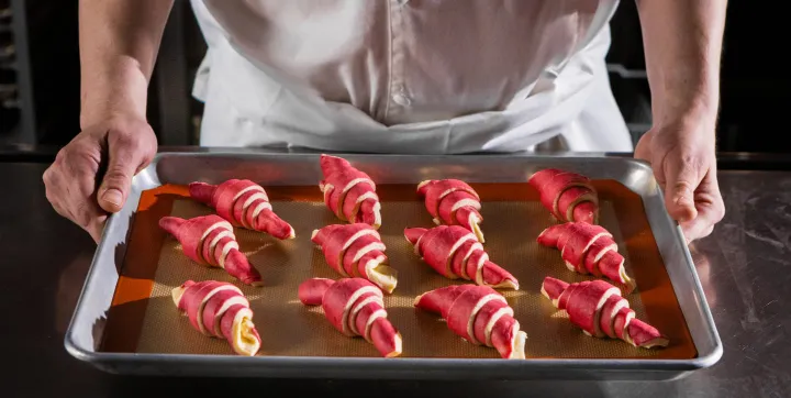 pastry cook presents colorful croissants on baking sheet