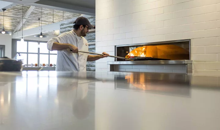 A chef places pizza into a Wood Stone wood fired oven