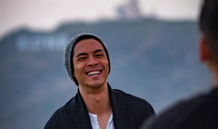 A man smiles in front of the Hollywood Hills in Los Angeles, photo by Sherman Yang via Unsplash